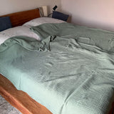 Couverture vert sauge dépliée sur un lit